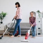 Beautiful,Housewife,Tiding,Floor,With,Canister,Vacuum,While,Little,Daughter